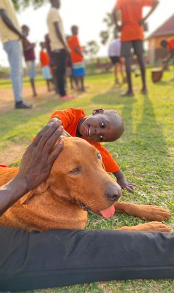 Ein lächelndes Kind streichelt einen sitzenden braunen Hund im Freien.