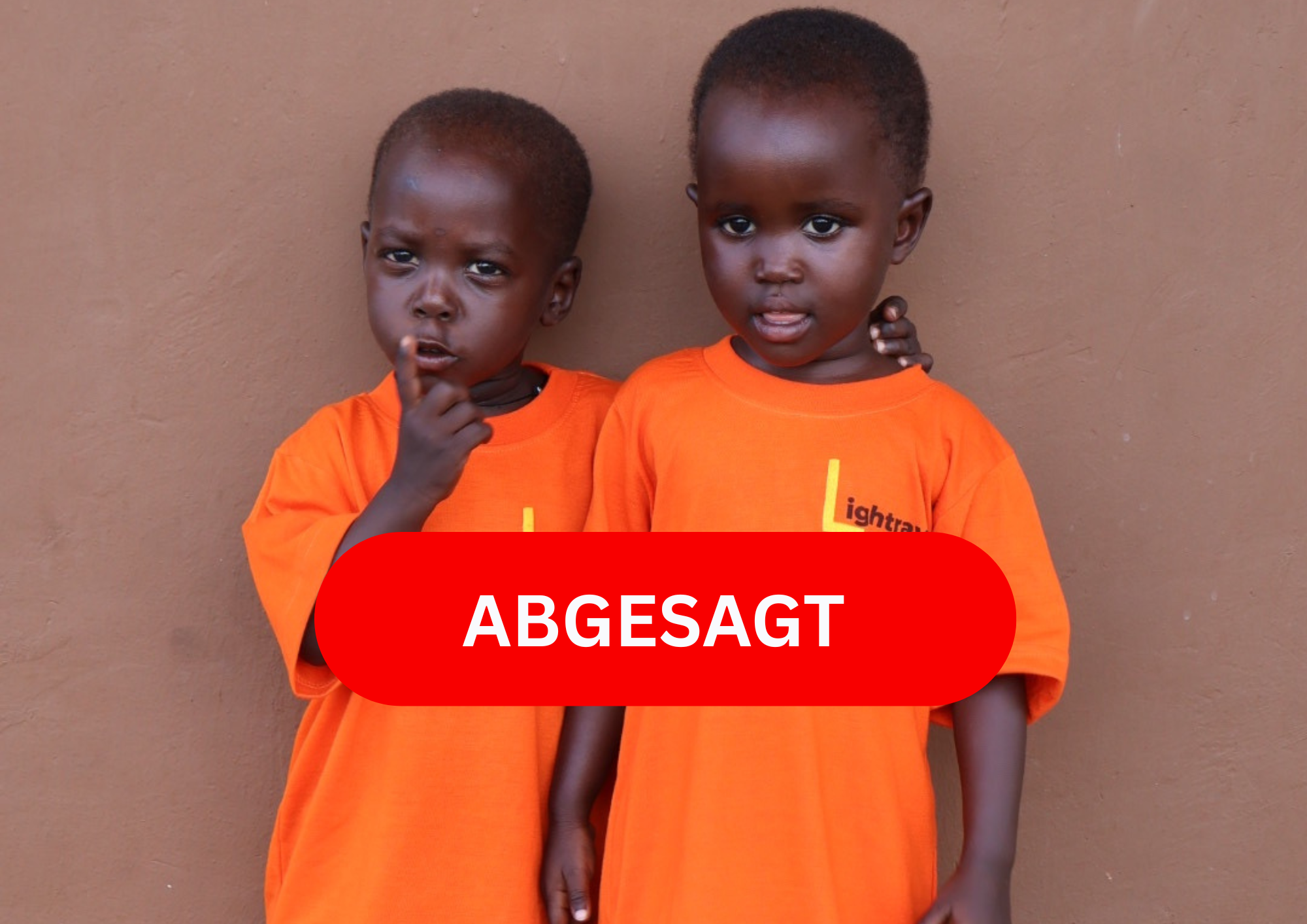 Zwei Kinder in orangefarbenen T-Shirts mit ernsten Gesichtern vor einer braunen Wand.