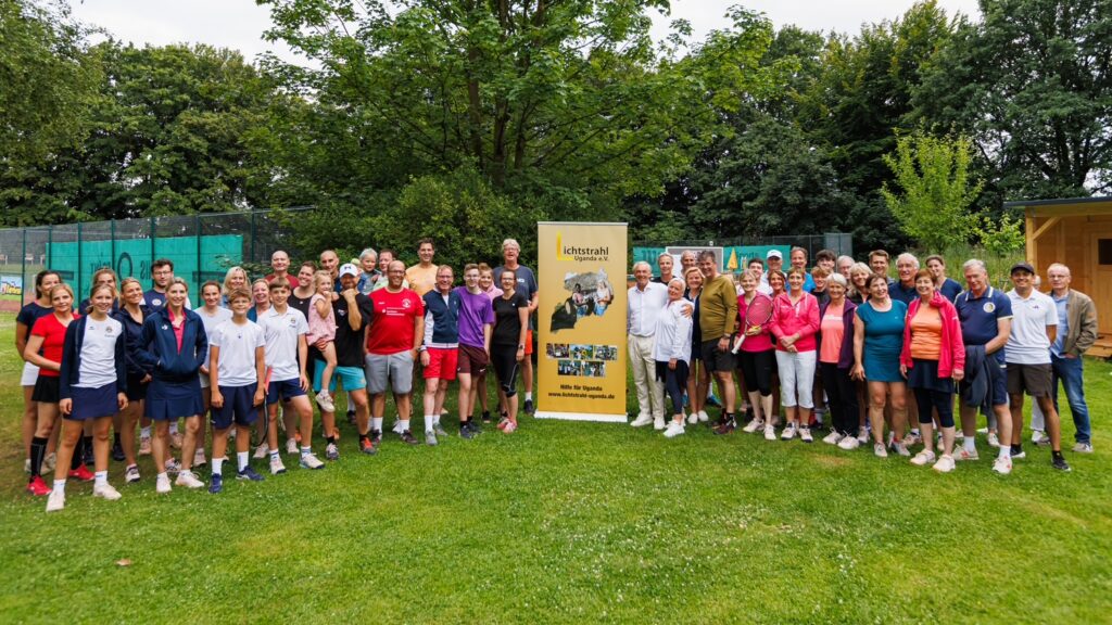 Eine Gruppe von Menschen in Sportkleidung steht lächelnd auf einem Tennisplatz neben einem Banner.