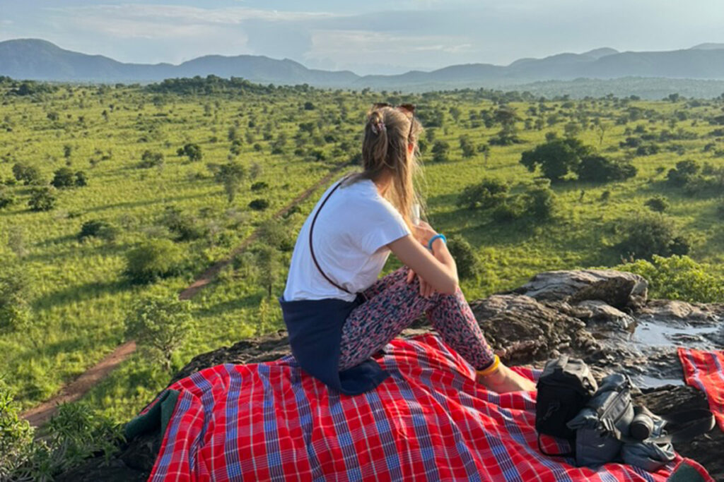 Eine Frau auf einer Decke schaut nachdenklich in die grüne Landschaft mit Bergen.