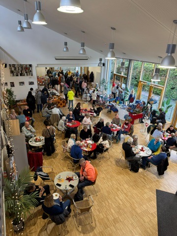 Viele Menschen sitzen entspannt an runden Tischen in einem hellen Cafebereich