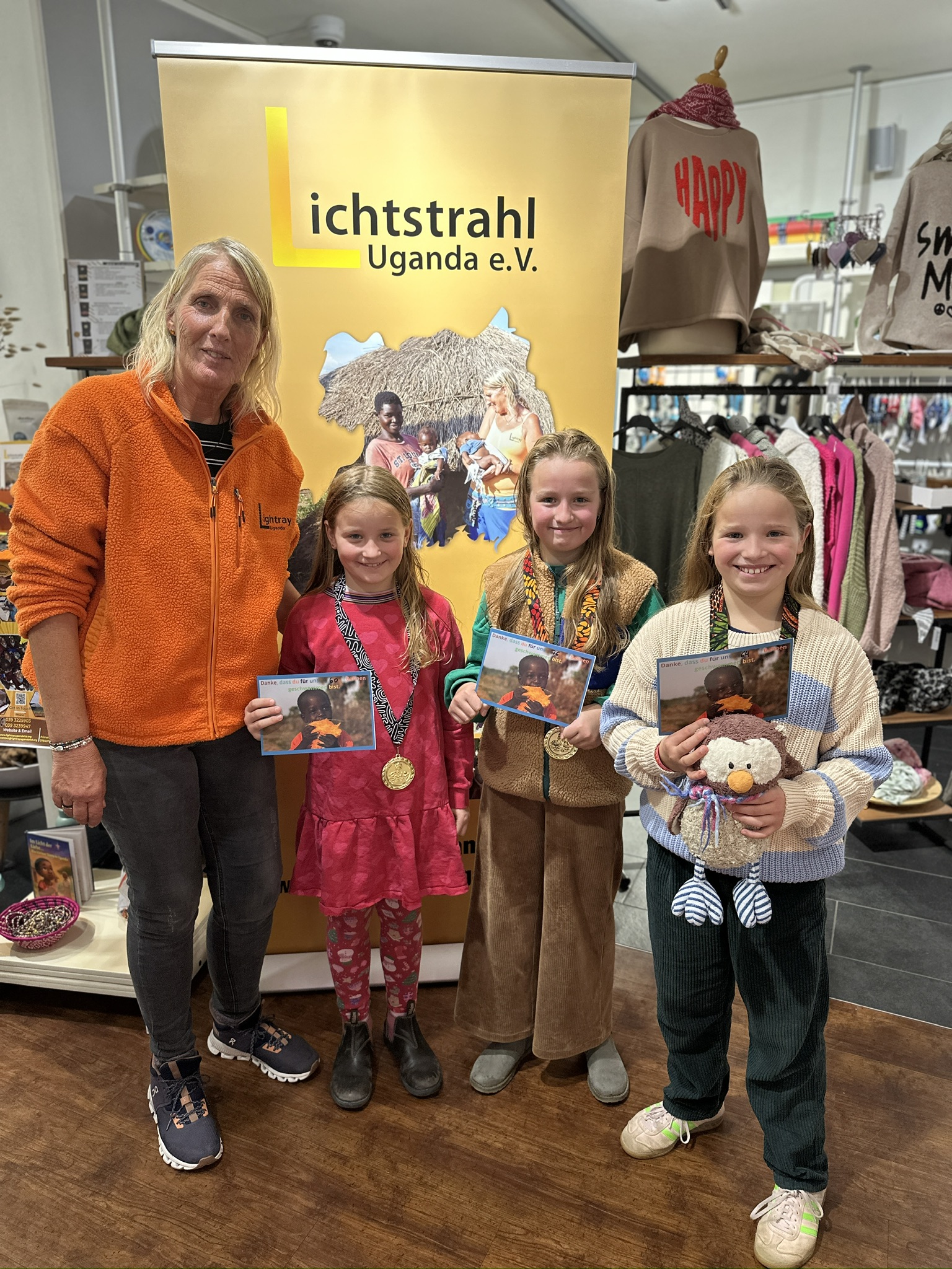 Vier Mädchen stehen fröhlich vor einem Lichtstrahl Uganda e V Banner im Laden