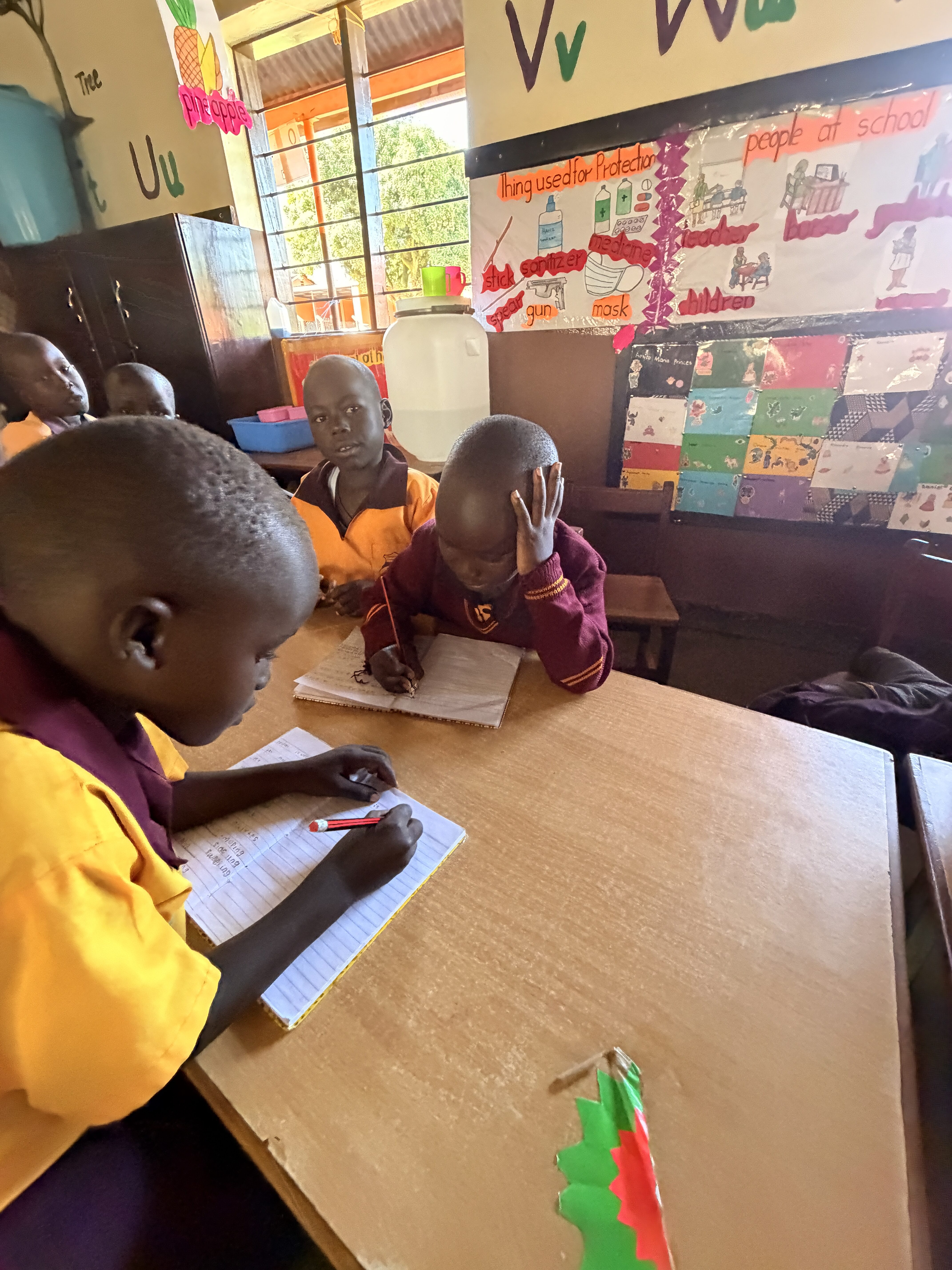 Kinder mit ernsten Gesichtern schreiben in Hefte am braunen Tisch im bunten Klassenzimmer