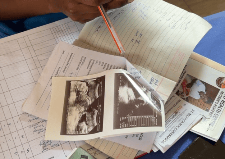 Hand mit Stift, konzentriert über Dokumenten, blauem Tisch und Ultraschallfoto