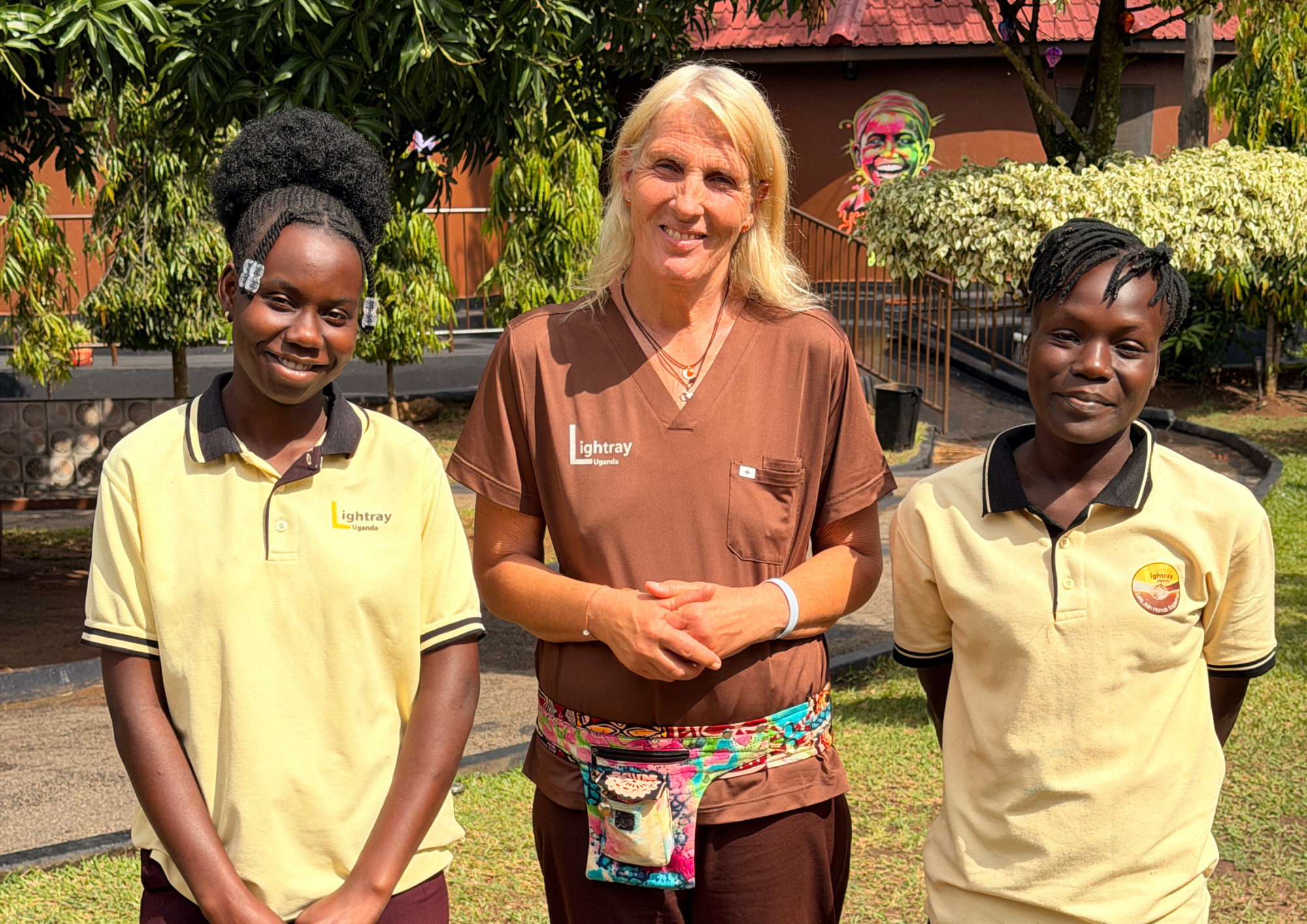 Drei laechelnde Frauen in Lightray Uganda Kleidung stehen im Freien zusammen